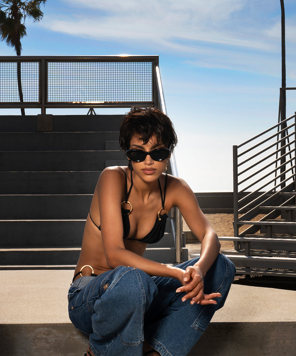 Model wearing a black swim top and black sunglasses.